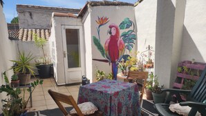 Eine Terrasse mit Tisch, Stühlen, Blumentöpfen und einem Wandbild eines Papageis.
