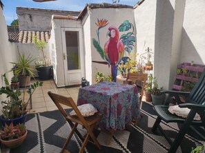 Eine Terrasse mit Tisch, Stühlen, Blumentöpfen und einem Wandbild eines Papageis.