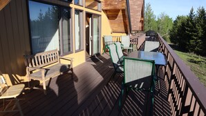 Een houten terras met tuinmeubilair, een glazen deuropening en uitzicht op bomen.