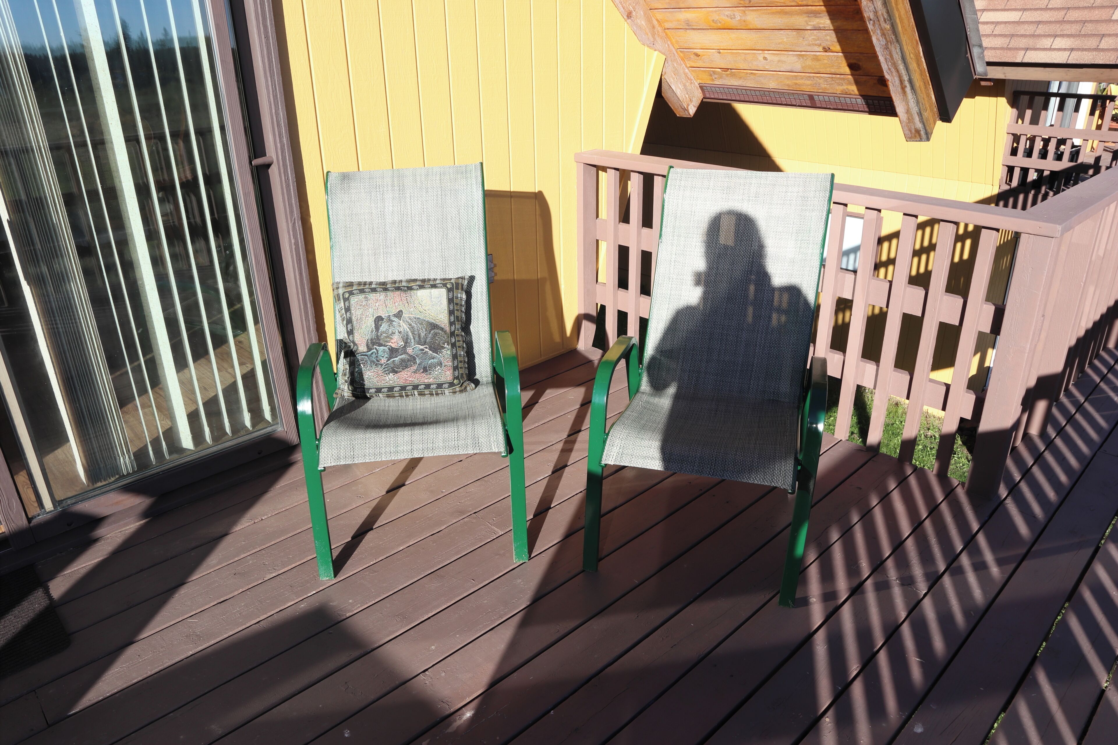 Une terrasse en bois avec deux chaises et une petite table, une rambarde en bois et un mur jaune.