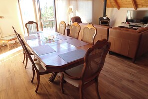 A dining area with a wooden table and chairs, a television, and a wood-burning stove.