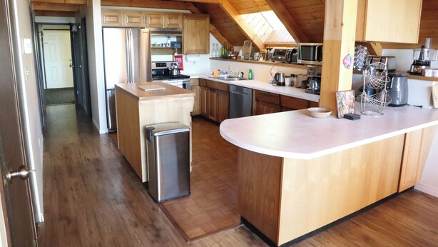 Een keuken met houten kastjes, een centraal eiland, roestvrijstalen apparatuur en een zichtbare deur naar een andere kamer.