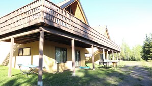 Een houten chalet met twee verdiepingen en een overdekte veranda, met daaraan een klein tafeltje.