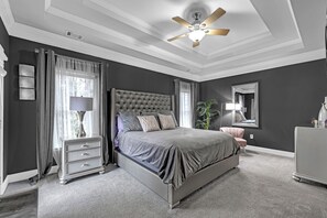 Ein Schlafzimmer mit einem großen Bett, einem Nachttisch, einer Lampe, einem Deckenventilator und einem Spiegel.