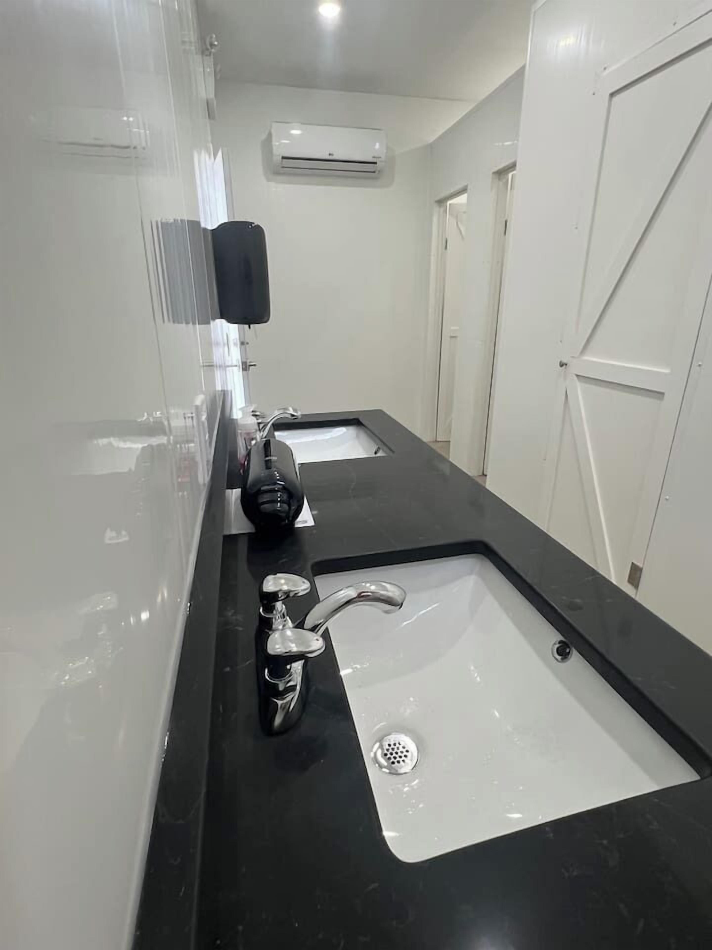A modern bathroom with two sinks, a hand dryer, and an air conditioning unit.