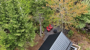 A wooden cabin with a black roof, surrounded by trees and a gravel path. - Cozy Loft Bunkie | Sleeps 4 | BBQ + Fire Pit (Mount Uniacke)