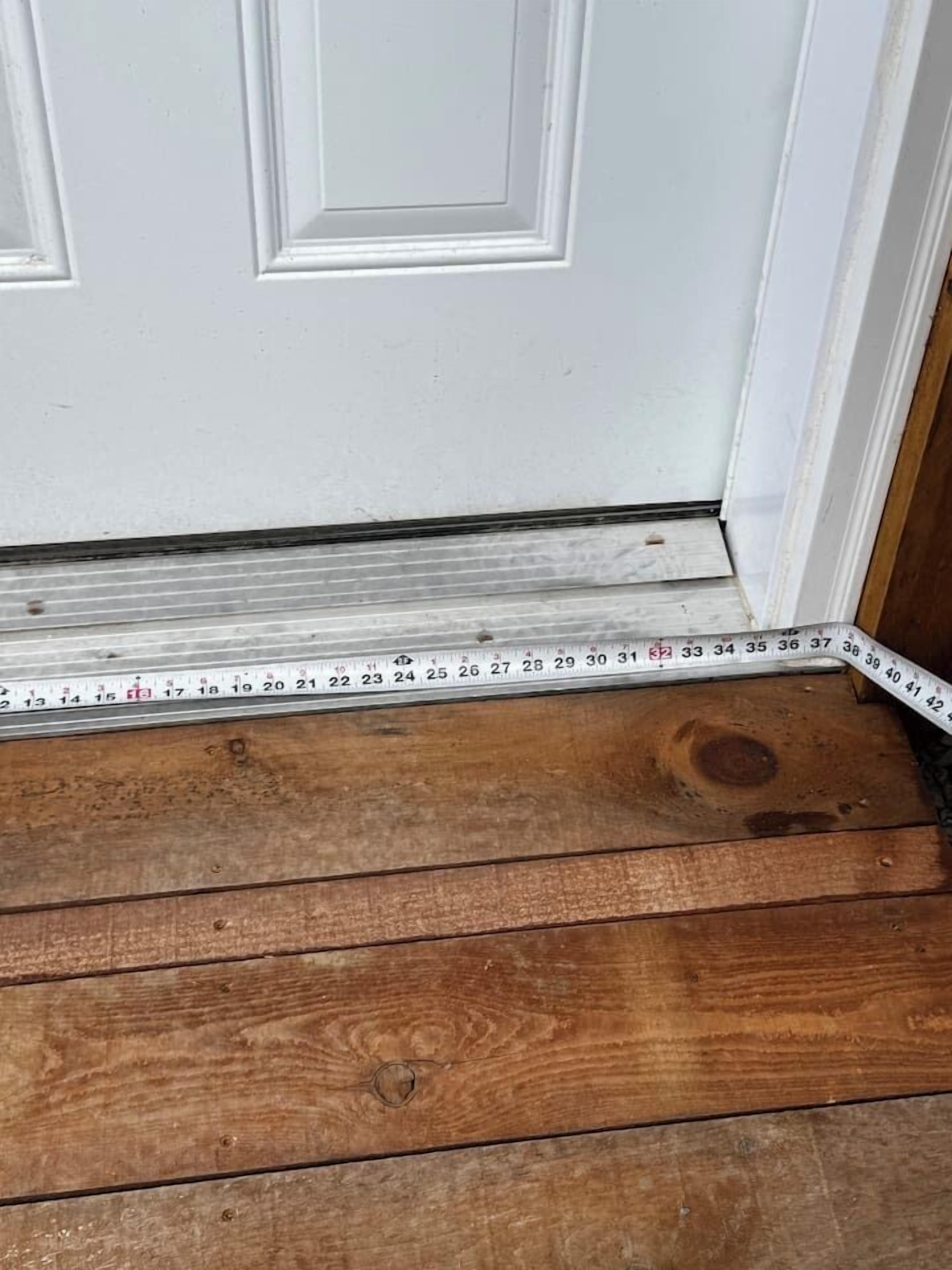 A wooden floor leading to a white door with a measuring tape placed on it.