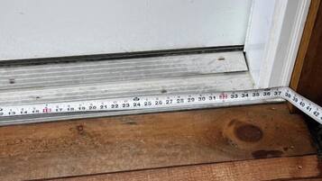 A wooden floor leading to a white door with a measuring tape placed on it.
