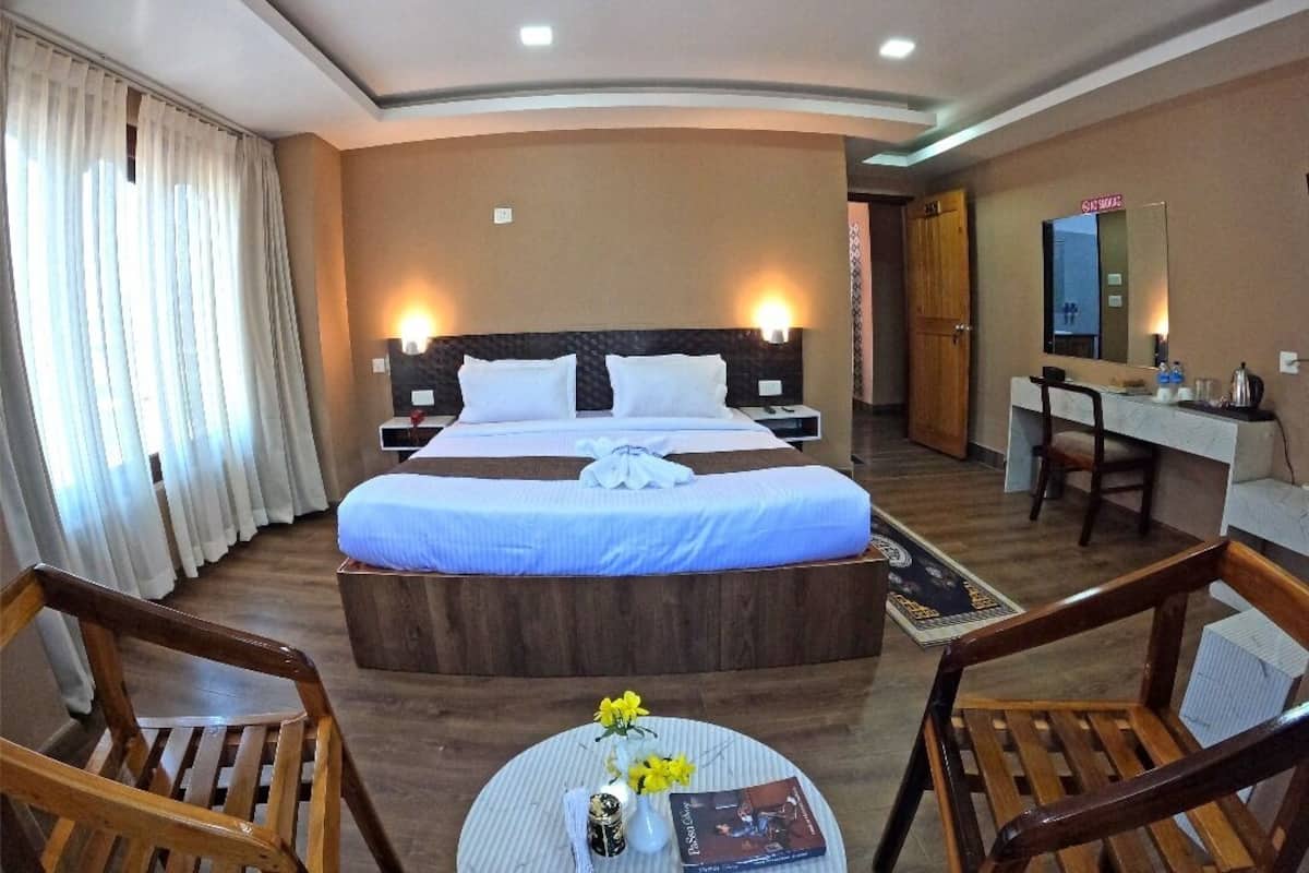 Habitación de hotel con una cama grande, un escritorio, dos sillas y una mesita con flores.