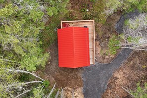 A red-roofed structure with a wooden frame, surrounded by greenery and a dirt path. - Romantic Nature Stay | Accessible Cabin for 2 (Mount Uniacke)