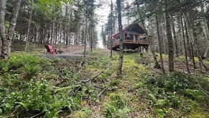 A cabin in a forest with a deck and a red chair.