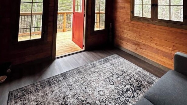A log cabin interior with a large window, a red door, and a gray sofa.