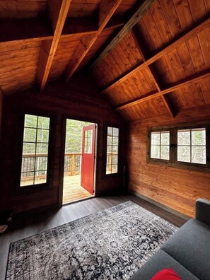 A log cabin interior with a large window, a red door, and a gray sofa.