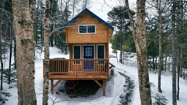 Una cabaña de madera con balcón, rodeada de árboles y nieve.
