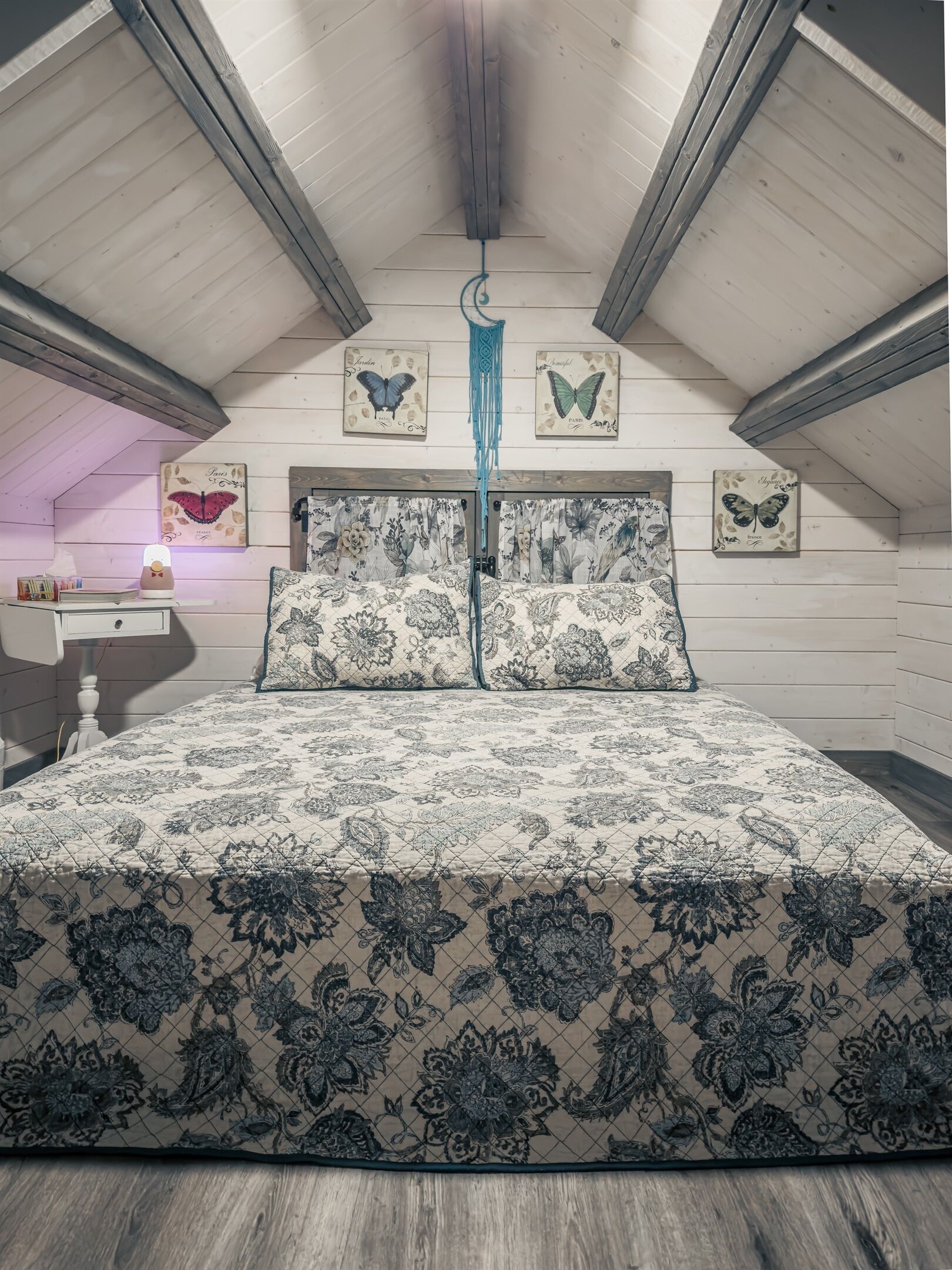 Une chambre à coucher avec une couvre-lit à motifs, des poutres en bois au plafond et des décorations murales sur le thème des papillons.