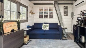 Una habitación acogedora con un sofá azul, un aparador de madera, una cafetera y una escalera.