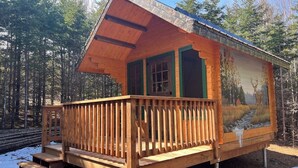 A wooden cabin with a balcony, a painting of a landscape on the side, and a set of stairs leading to the entrance. - Pet-Friendly Cabin | Sleeps 2 | Private Fire Pit (Mount Uniacke)