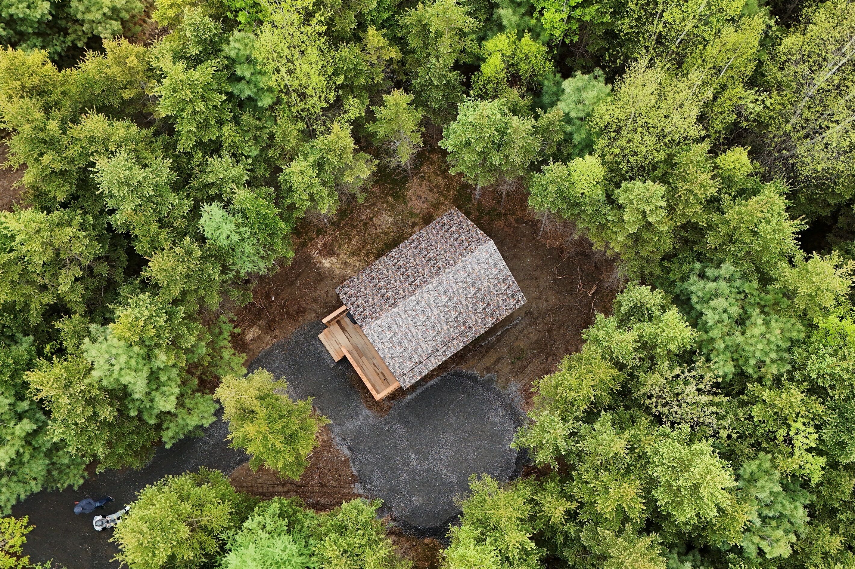A small, rectangular building with a sloped roof surrounded by dense green trees.