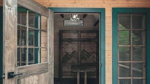 A wooden cabin with a large open door, a small table, and a hanging light fixture. - Pet-Friendly Cabin | Sleeps 2 | Private Fire Pit (Mount Uniacke)