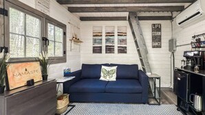 A cozy room with a blue sofa, a wooden cabinet, a coffee machine, and a staircase. - Private 4 Cabin Retreat | Hot Tub | Tiny Cabins (Mount Uniacke)