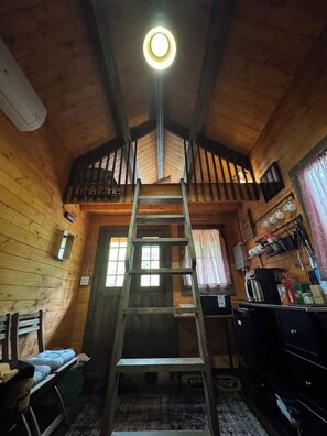 L’intérieur d’une cabane en bois est doté d’une échelle en bois centrale, d’une petite fenêtre et d’un coin cuisine.