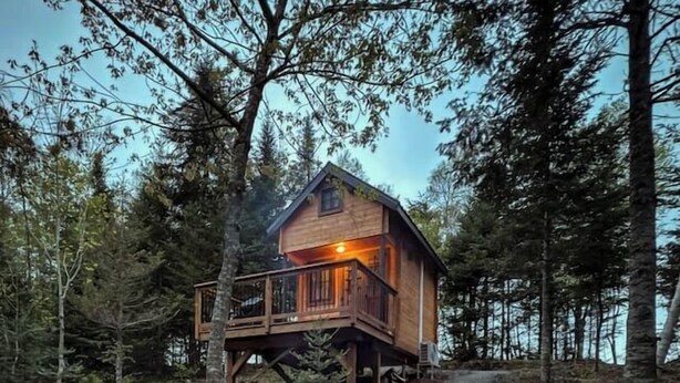 A cabin with a deck, two red Adirondack chairs, and a fire pit. - Private 4 Cabin Retreat | Hot Tub | Tiny Cabins (Mount Uniacke)