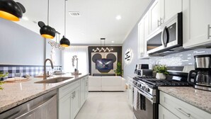 A modern kitchen with a central island, stainless steel appliances, and pendant lighting. - Immersive Rooms • Gaming Lounge • Summerville (Kissimmee)