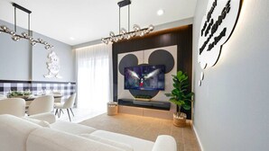 A modern living room with a flat-screen TV, white sofas, a dining area with a checkered tablecloth, and a decorative wall piece. - Immersive Rooms • Gaming Lounge • Summerville (Kissimmee)