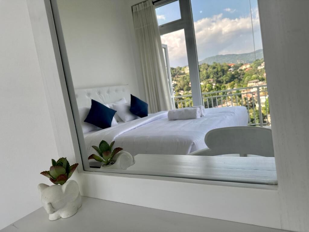 A bedroom with a bed, pillows, a nightstand, a plant, and a window with a view of a cityscape.