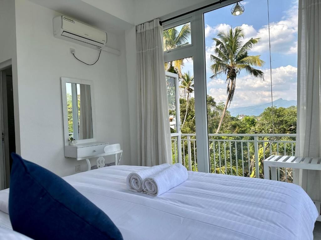 Ein Hotelzimmer mit Bett, Spiegel, Klimaanlage und einem Balkon mit Blick auf Palmen und Berge.