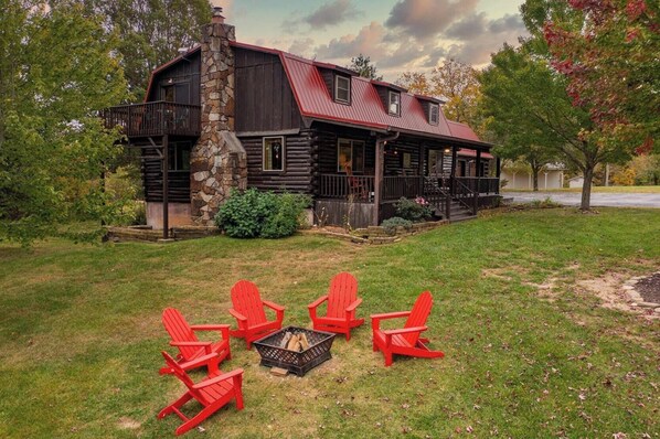 A log cabin with a stone chimney, a porch, and a fire pit with chairs. - Ozark Private Cabin, sleeps 12, on 6+ acres, Close to Dogwood Canyon & Branson (Lampe)