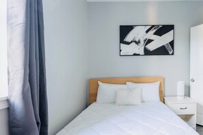 A hotel room with a bed, a nightstand, a white cabinet, and a painting on the wall.