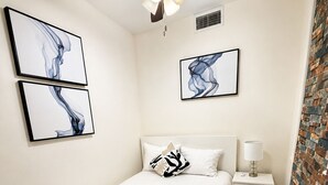 Ein Schlafzimmer mit Bett, Nachttisch, Lampe, Deckenventilator, Kunstwerk und einem gemusterten Teppich.