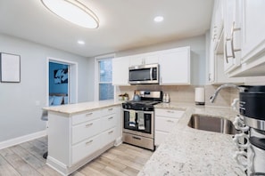 A modern kitchen with white cabinetry, a stainless steel sink, a microwave, an oven, and a granite countertop.