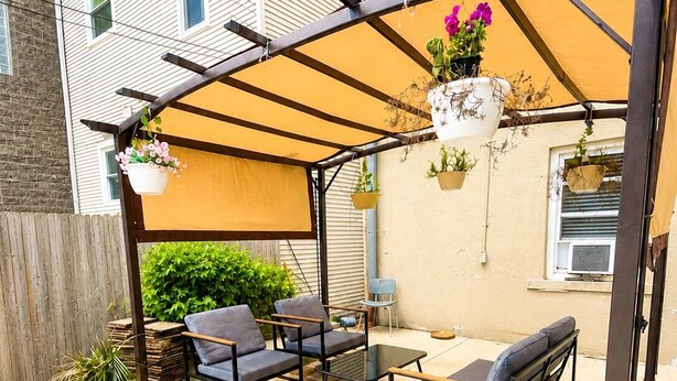 Ein überdachter Patio-Bereich mit Gartenmöbeln, einer Pergola und hängenden Pflanzgefäßen.