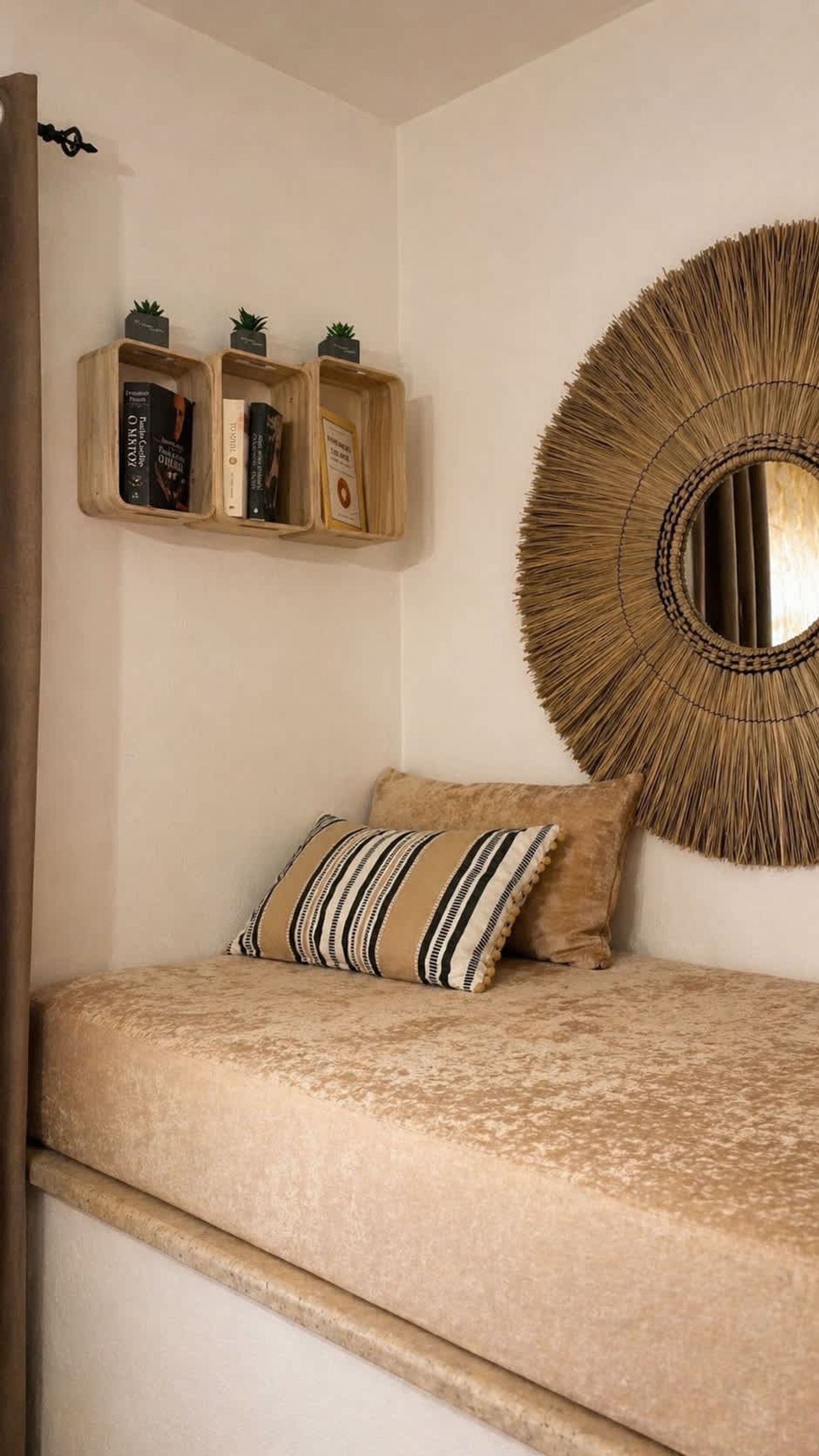 Quarto com cama, espelho redondo na parede e prateleira de madeira com livros e pequenas plantas.