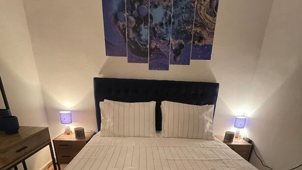 Una cama bien hecha con ropa de cama a rayas, dos mesitas de noche con lámparas, y una pared decorada con cuatro cuadros.