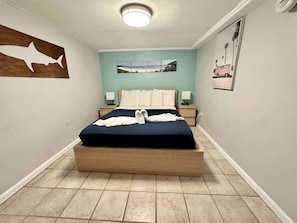 A bedroom with a bed, a wall-mounted shark silhouette, a landscape painting, and a pink car illustration. - Apto 1E Flamenco Beachfront Villas (Flamenco)