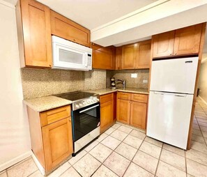 Una cocina con armarios de madera, un microondas, una estufa y un refrigerador.