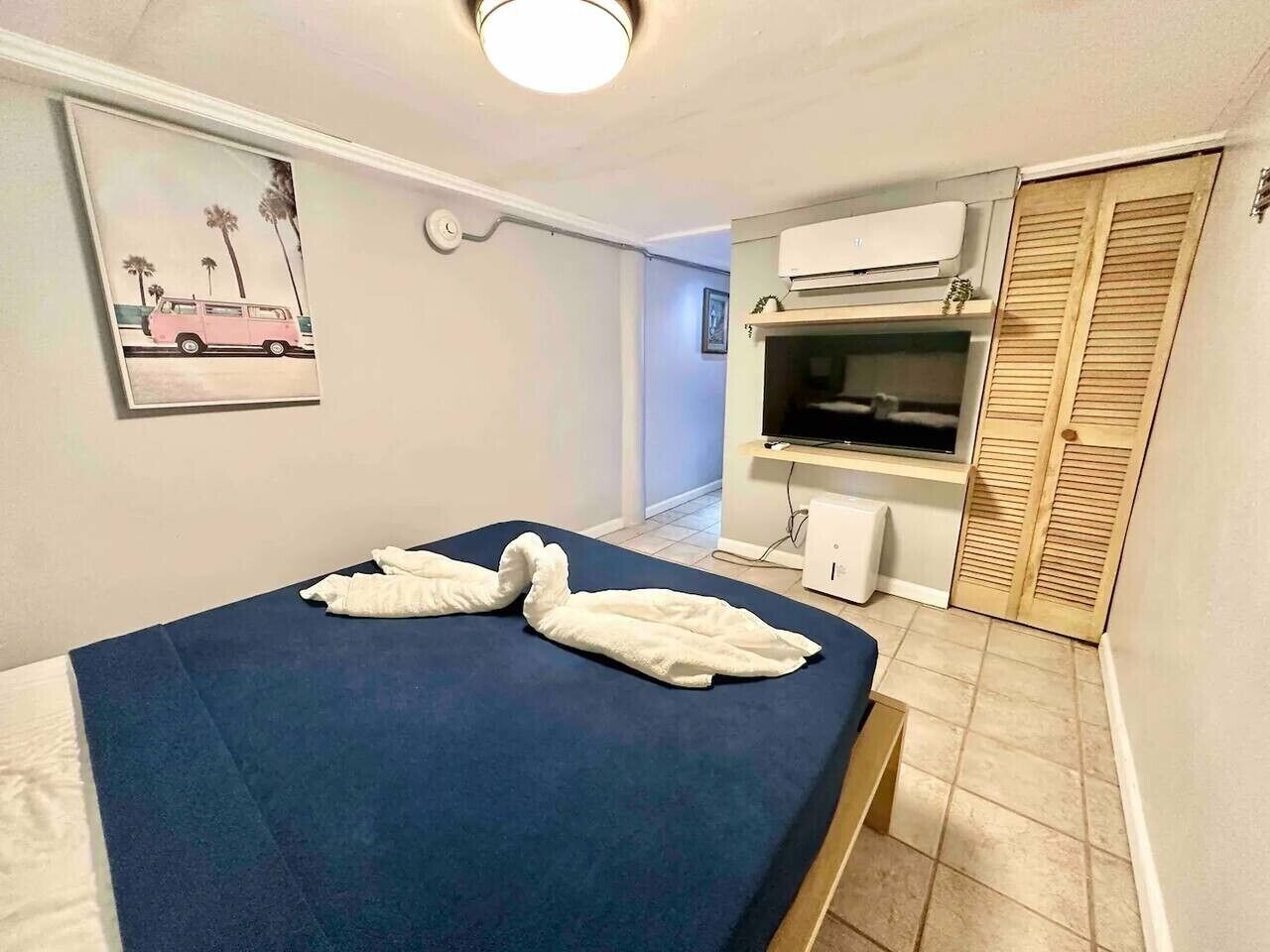 Une petite pièce comprenant un lit, un téléviseur, un climatiseur et une porte en bois.