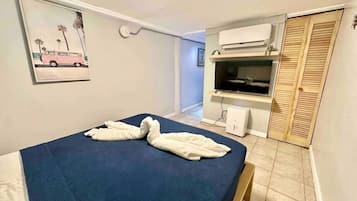 Une petite pièce comprenant un lit, un téléviseur, un climatiseur et une porte en bois.