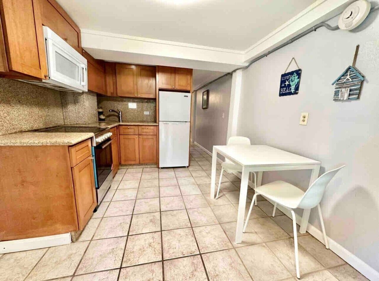 A compact kitchen with wooden cabinets, a white refrigerator, and a small dining table with white chairs.