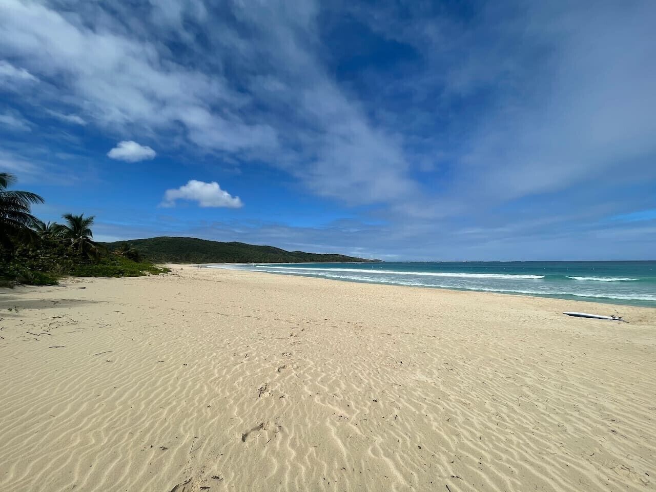 Una playa con arena, océano y colinas a lo lejos.