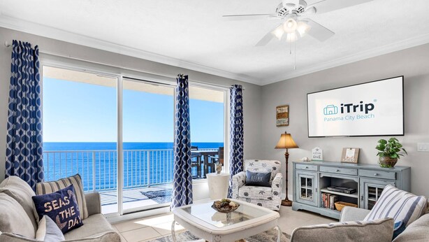 Un salon avec vue sur l’océan, un ventilateur de plafond et une enseigne indiquant « iTrip Panama City Beach ».