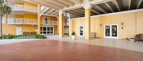 A spacious outdoor area with a red-tiled floor, yellow walls, and a covered section with white railings.