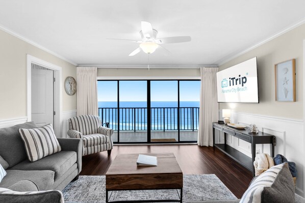 Ein Wohnzimmer mit Sofa, Sesseln, Couchtisch und Fernseher, der 'iTrip Panama City Beach' anzeigt.