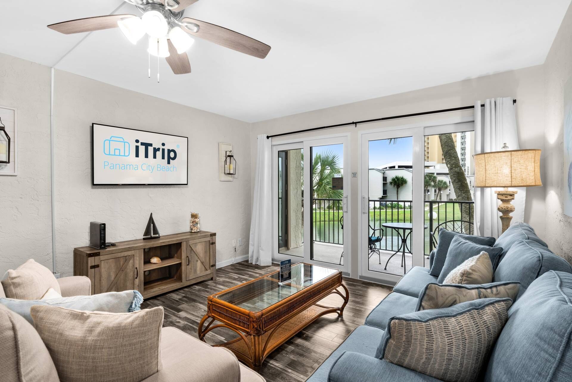 A spacious living room with a large sofa, a coffee table, and a ceiling fan. There is a sign on the wall that reads "iTrip Panama City Beach."