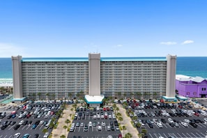 A large hotel with a parking lot in front, a beach view, and a clear sky. - Summit Beach Resort 1429 (Panama City Beach)