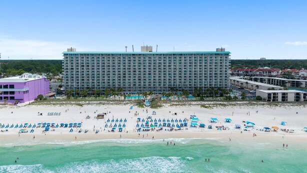 A large hotel with multiple floors, a beach with numerous umbrellas, and a clear view of the ocean. - Summit Beach Resort 1429 (Panama City Beach)
