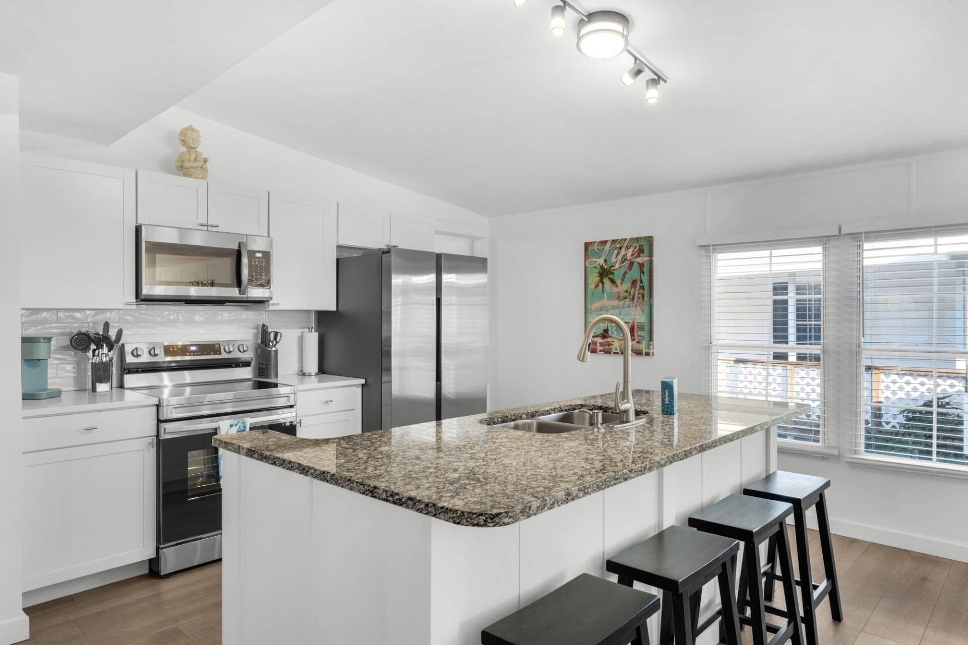 A modern kitchen with white cabinetry, stainless steel appliances, a granite countertop, and a small island with bar stools.